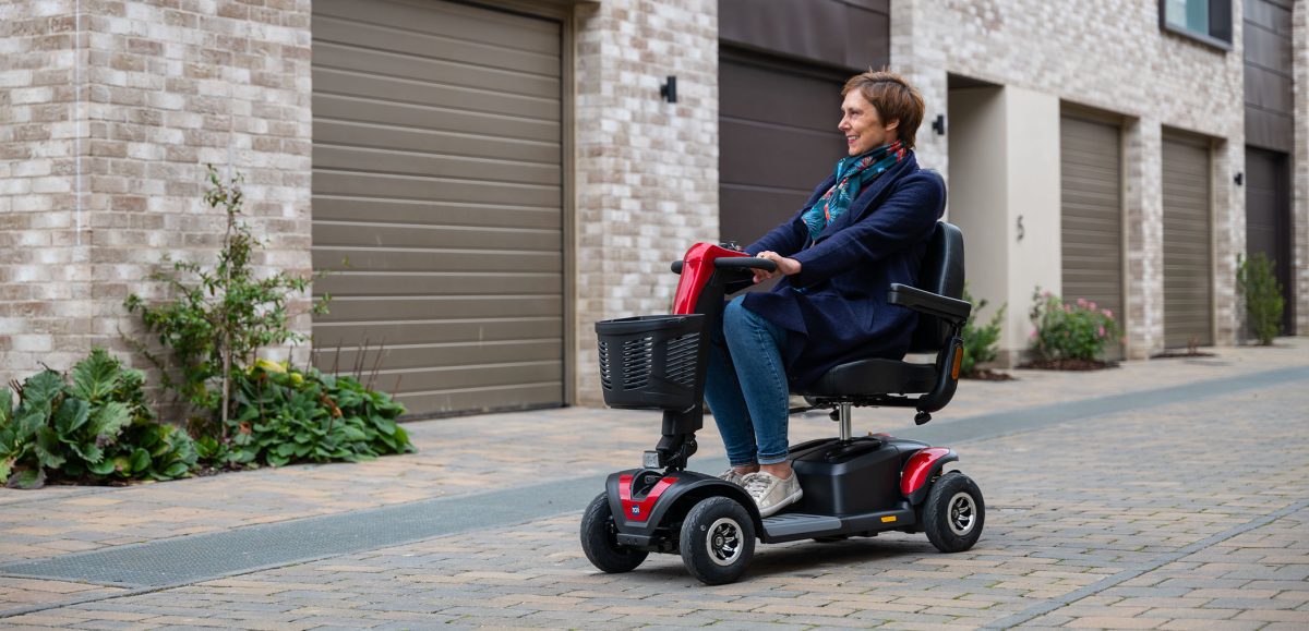 A woman driving a lightweight mobility scooter on a wide pavement