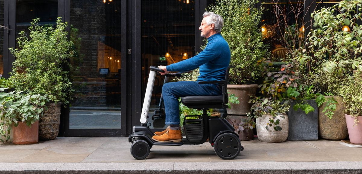 A man riding a mobility scooter on the pavement next to a florists