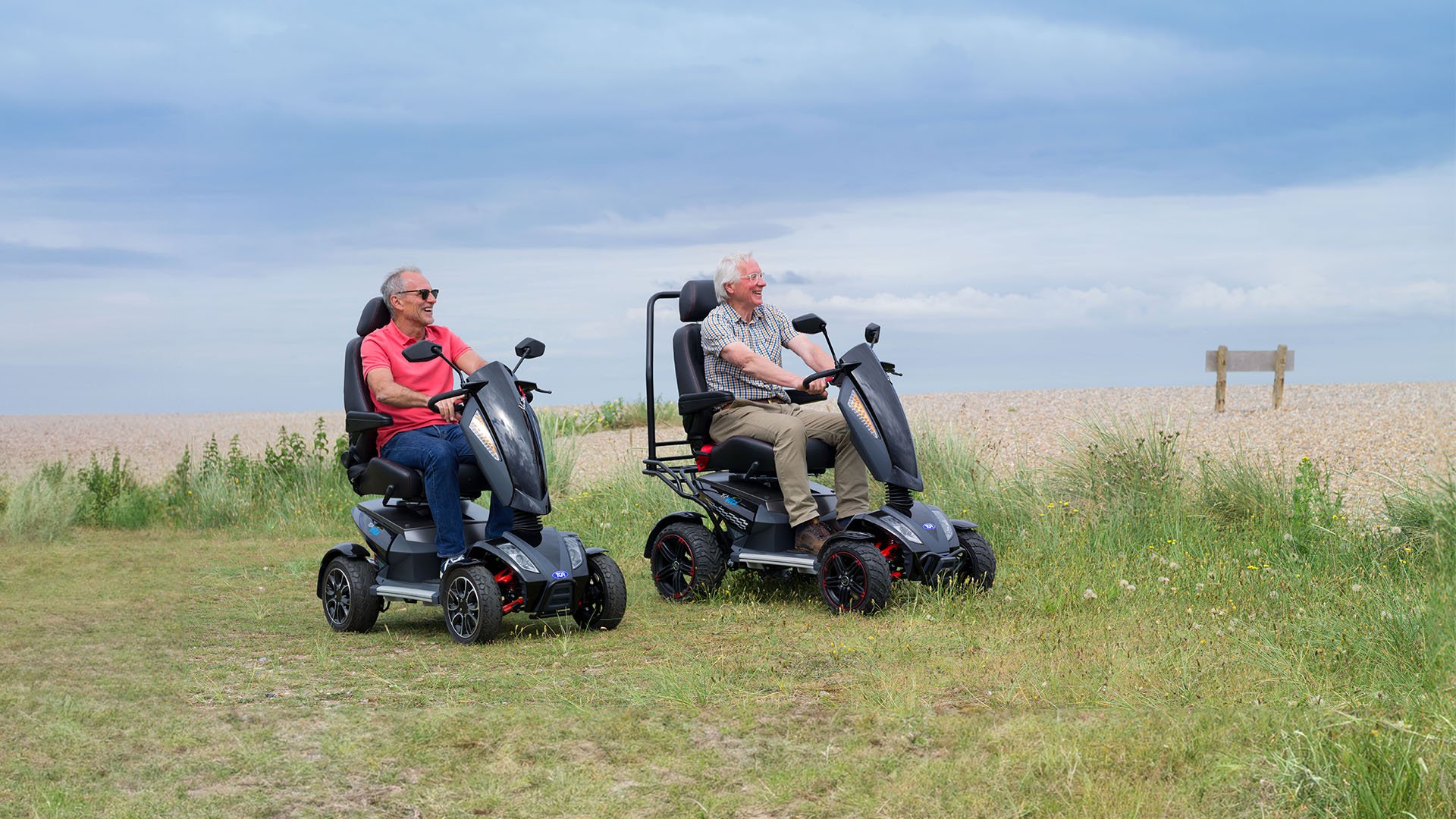 A man and a woman on TGA mobility scooters by the seaside