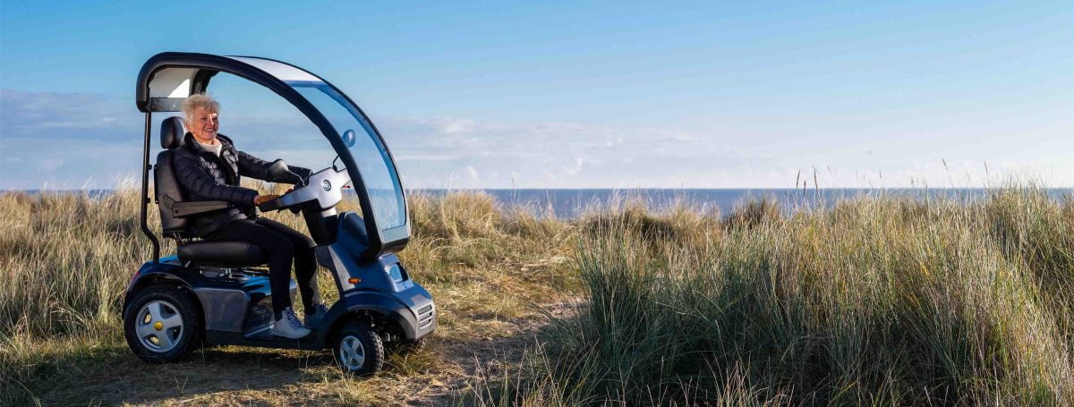 A person using a mobility scooter with a canopy on a beach by the sea